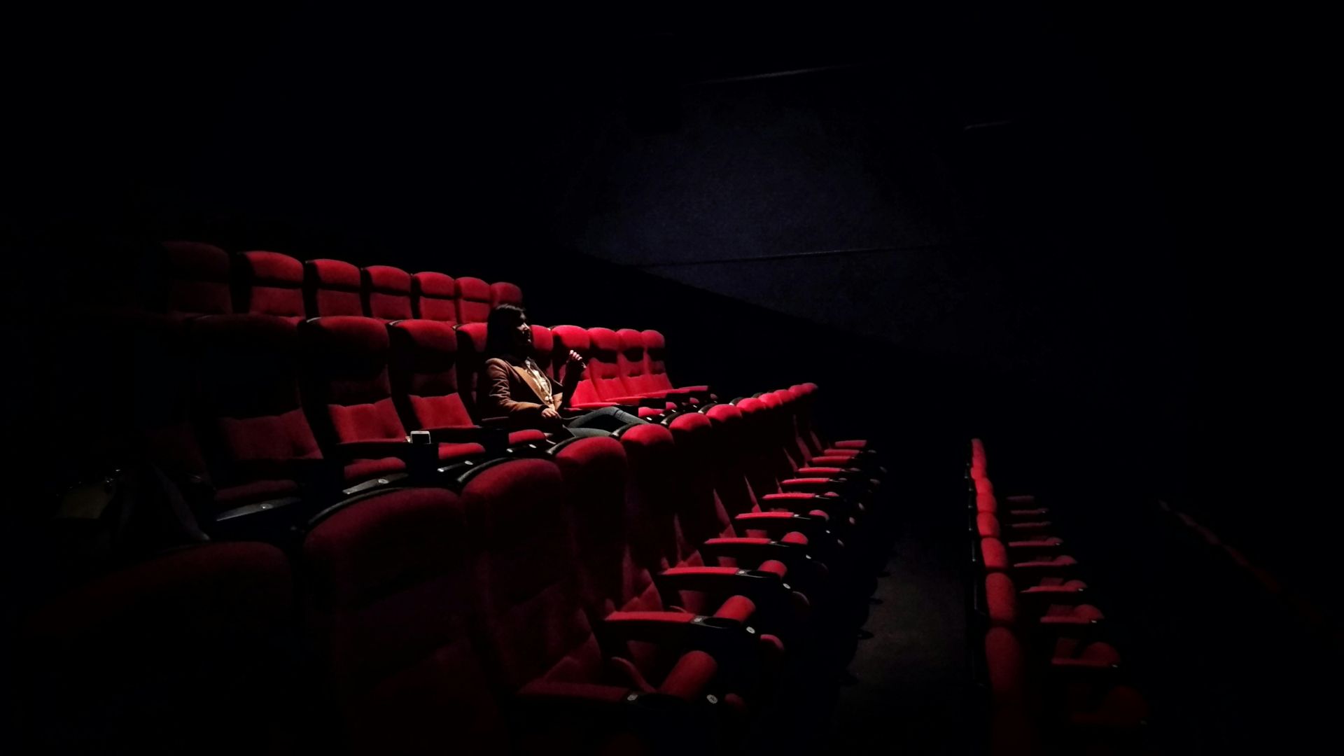 A dark cinema hall with a single person sitting silently as the movie screen glows softly, showing the power of silence in movies