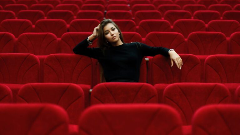 An exhausted woman sitting alone in a movie theater, reflecting emotional fatigue caused by modern movies